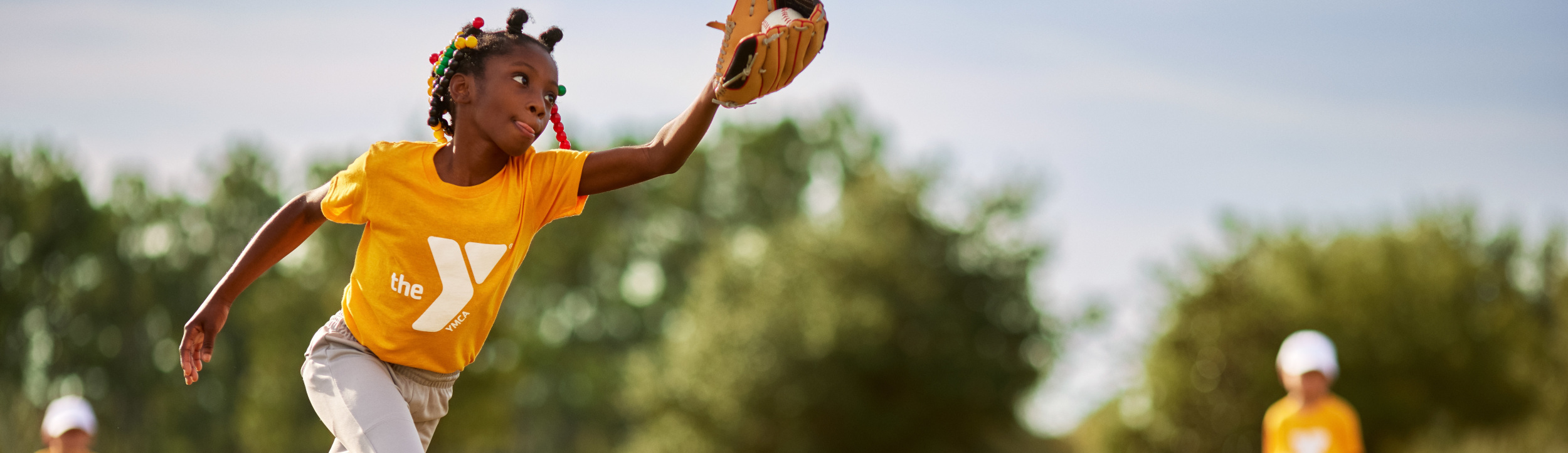 Young girl in yellow shirt catching ball in mitt.