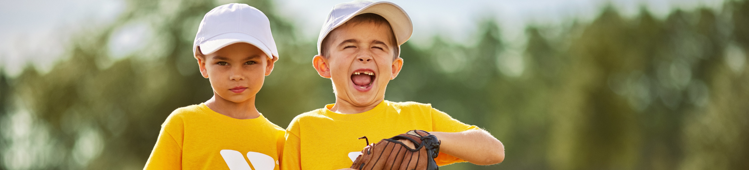 Two little boys playing baseball smiling at the camera.